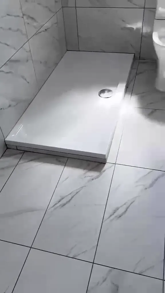 Large-format marble-effect floor tiling around a shower tray.